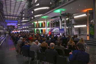 In der Halle des Paul-Löbe-Haus sitzen zahlreiche Teilnehmende in Stuhlreihen