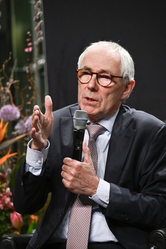 Der Herr in Anzug und Krawatte spricht auf der Bühne, er gestikuliert Richtung Publikum