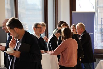 Etwa 10 Personen unterhalten sich an Stehtischen im Pausenbereich.