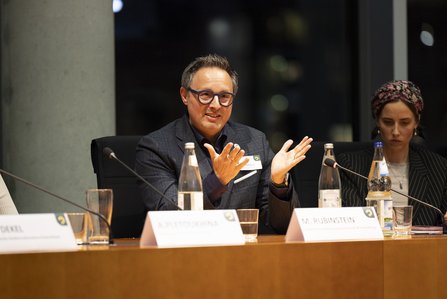 Man (Michael Rubinstein) spricht, Hände offen nach oben gerichtet