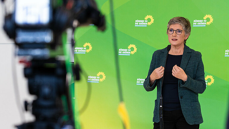 Britta Haßelmann vor einem grünen Banner mit Logos der grünen Bundestagsfraktion.