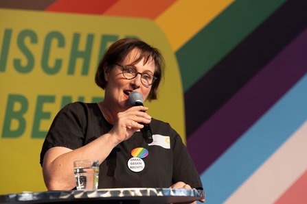 Eine Frau mit Mikro vor dem Bühnenhintergrund, angeschnitten der Schriftzug Parlamantarischer Regenbogenabend