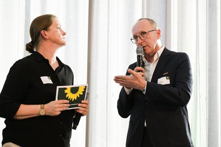 Frau mit Moderationskarte in der Hand blickt auf sprechenden Mann mit Mikroim Gespräch mit Mann