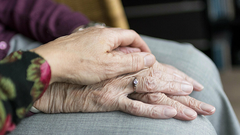 Eine Hand einer jüngeren Frau liegt auf der Hand einer älteren Frau.