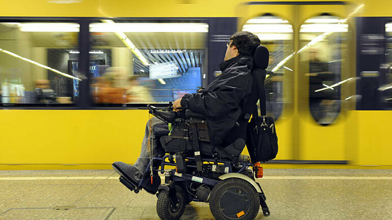Gehbehinderter Mann in einem Elektrorollstuhl an einer Stadtbahnhaltestelle in Stuttgart