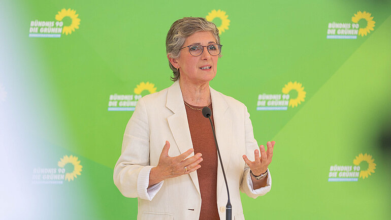 Britta Haßelmann, Fraktionsvorsitzende der Grünen im Bundestag, spricht vor einer grünen Wand mit Sonnenblumenlogo.