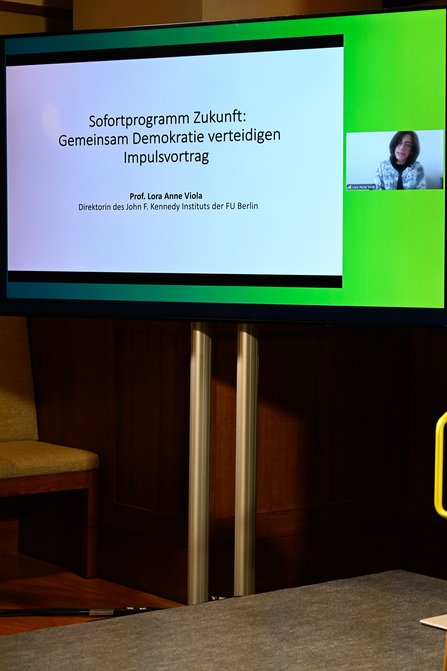 Auf einem Bildschirm ist eine Präsentation zu sehen, daneben ist der Kopf einer Frau eingeblendet