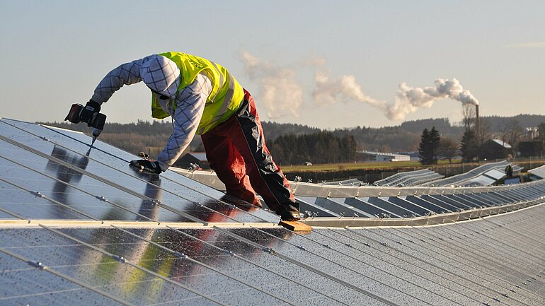 Ein Arbeiter verschraubt Solarpaneele.