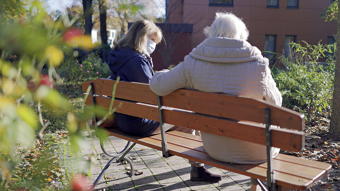 Pflegeheimbewohnerin sitzt mit Tochter auf einer Parkbank.