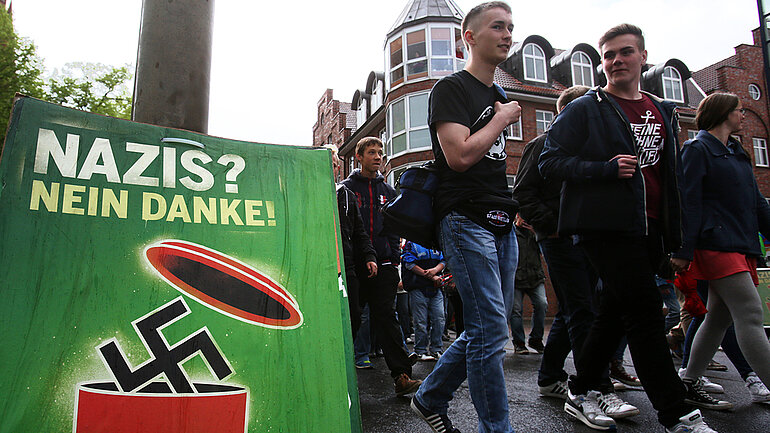 Junge Menschen laufen in einer Demo mit. Daneben ein Plakat mit der Aufschrift: Nazis? Nein danke!