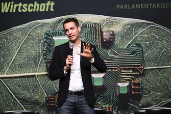 Ein Mann in Hemd, elegantem Jacket und Jeans spricht auf der Bühne