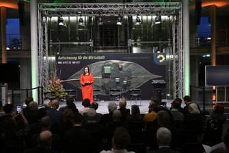 Auf der Bühne ist die Moderatorin in rotem Kleid