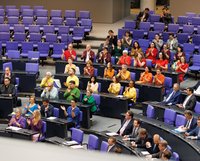 Die grüne Bundestagsfraktion sitzt im Plenarsaal in den Farben einer Regenbogenflagge.