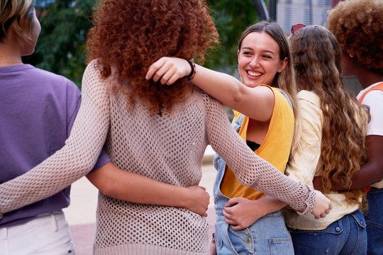 Mehrere Frauen stehen mit dem Rücken zur Kamera nebeneinander, die Arme verschränkt. Eine Frau schaut in die Kamera und lächelt