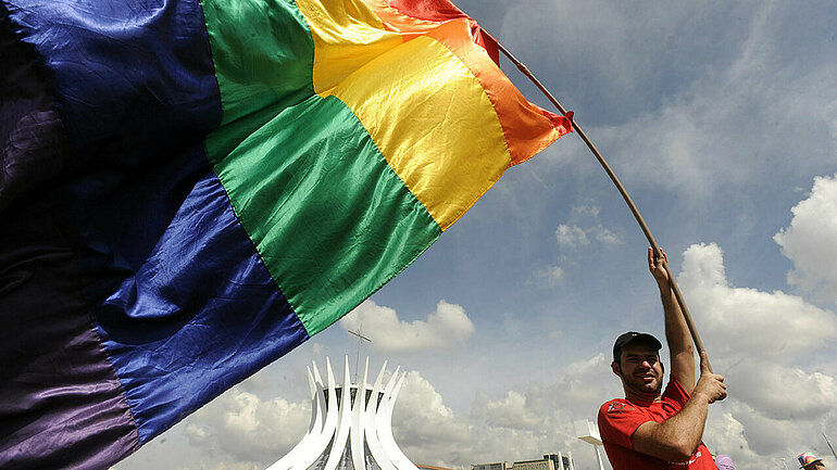 Ein Mann schwenkt eine Fahne in Regenbogenfarben