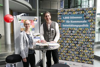 2 Personen vor dem Stand der Servicestelle Kommunen in der einen Welt. Links am Stand hängt ein roter Luftballon.