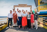 Grüne Bundestagsabgeordnete stehen lachend am Glasbahnhof Sassnitz auf Rügen.